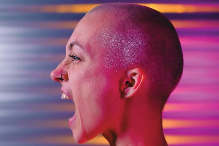 A woman with a shaved head is screaming in front of a colorful background during her photoshoot for a Product Design Agency in Swindon.